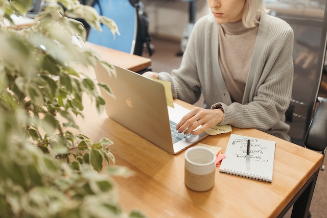 a blond landlord in a grey sweater researches rental market updates on their laptop while having a cup of coffee